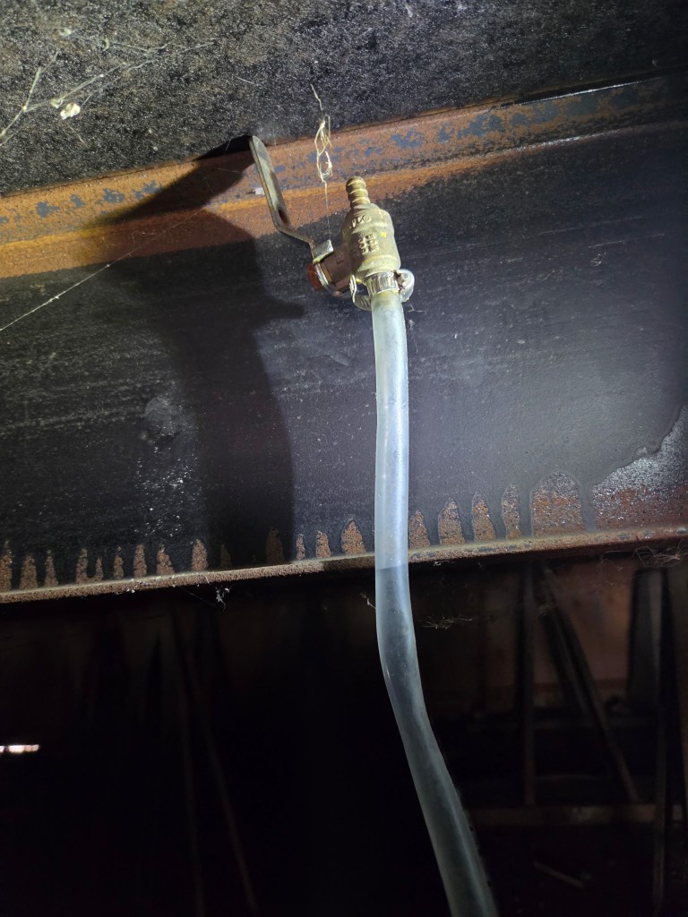 Water level hose reading elevation against a mobile home steel frame beam during an inspection