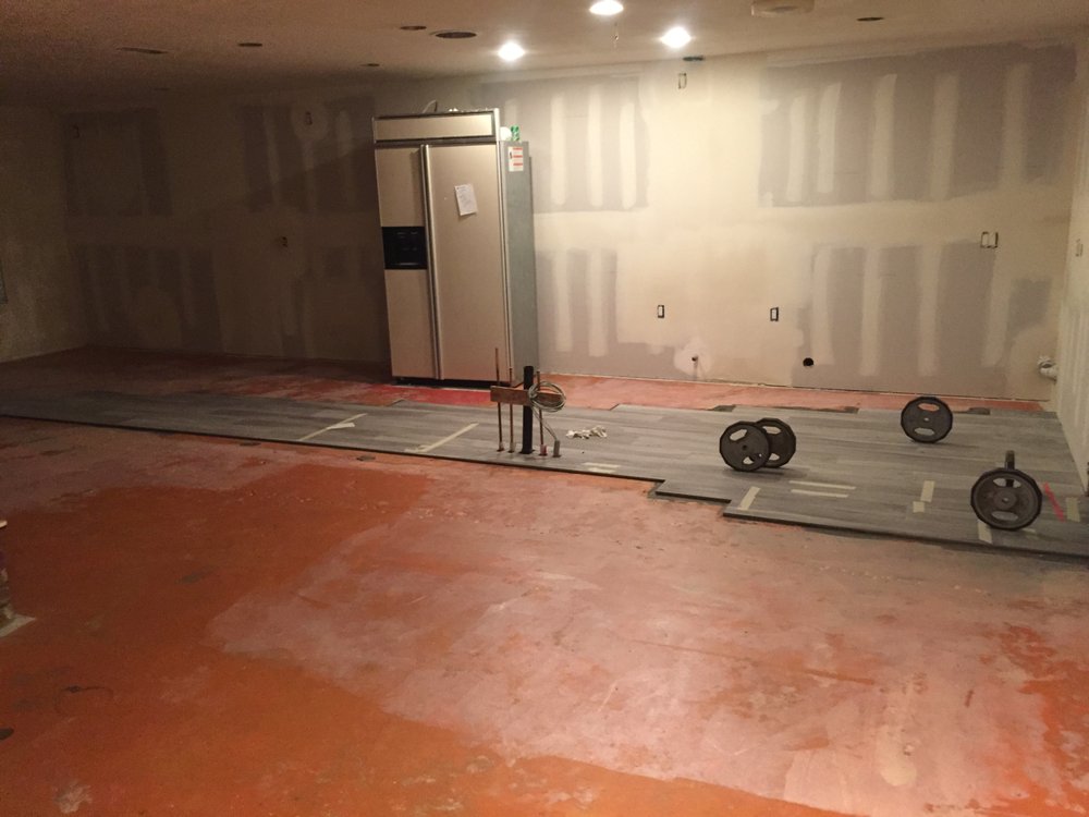 Vinyl plank flooring being installed over a prepared subfloor during a kitchen remodel