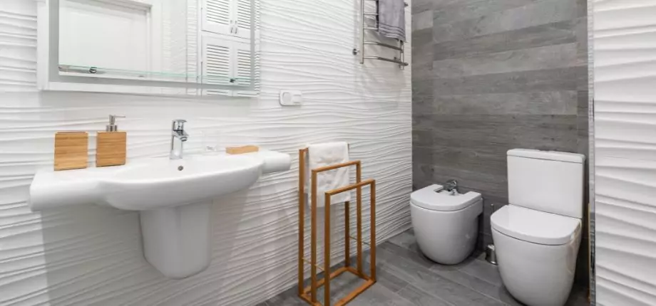 Modern bathroom interior with a wall-mounted sink, toilet, and bidet, featuring minimalist decor and textured walls.