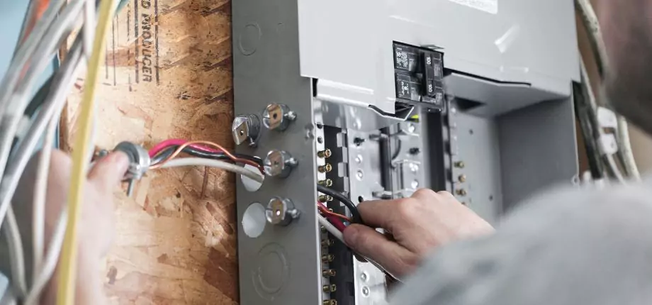 Electrician connecting wires in a circuit breaker panel, focusing on safe and accurate electrical installation.