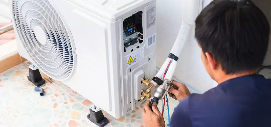 Technician installing an outdoor mini-split air conditioning unit, connecting refrigerant lines for efficient cooling
