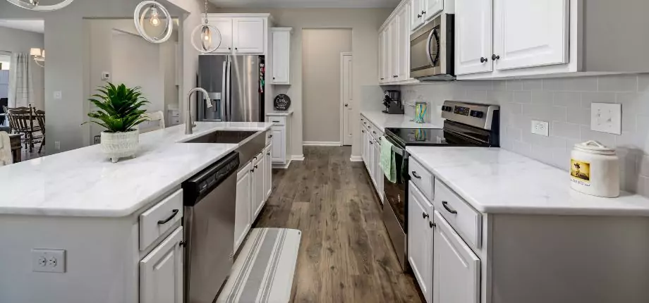 Modern kitchen with white cabinets, stainless steel appliances, and a spacious island, featuring a clean and open layout with wood flooring.