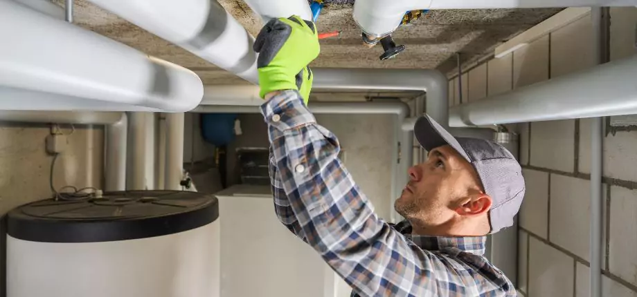 Plumber inspecting and repairing water pipes in a utility room, ensuring proper functionality and leak prevention.