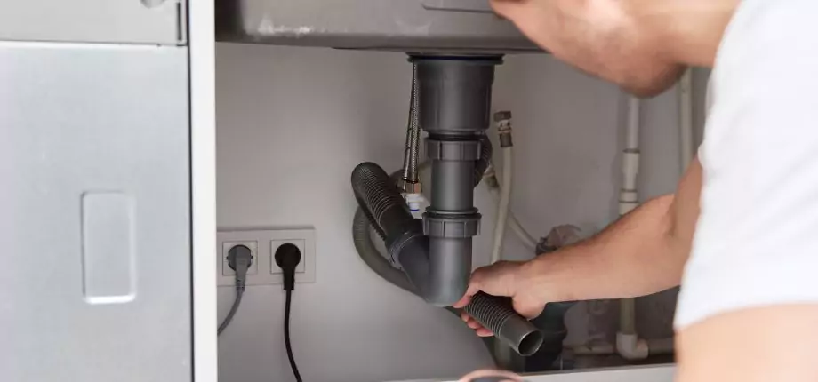 Plumber inspecting and adjusting drain pipes under a kitchen sink, ensuring proper drainage and leak prevention.