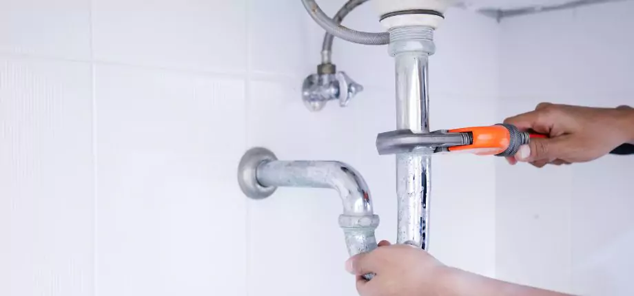 Professional plumber repairing a kitchen sink pipe with a wrench, showcasing plumbing service expertise.