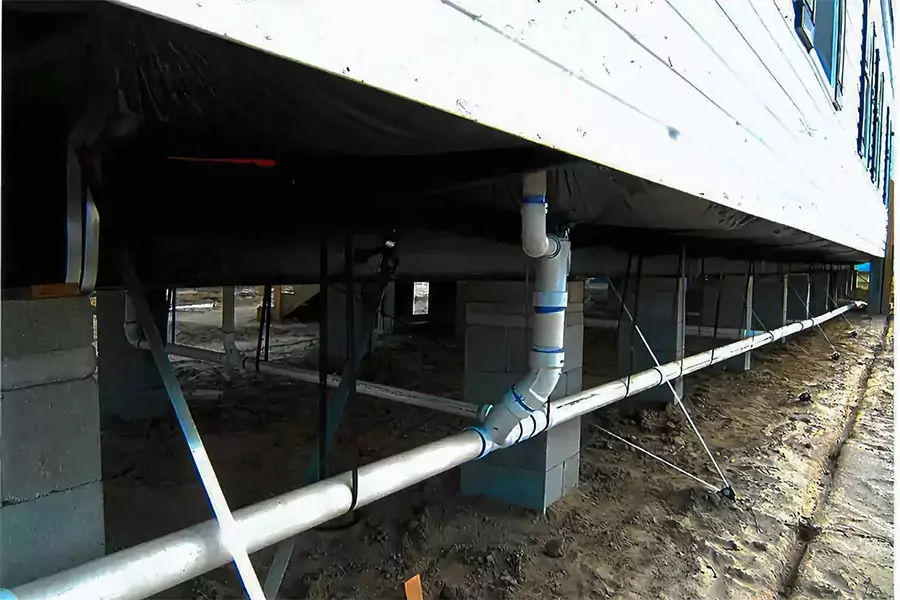 Underneath view of mobile home plumbing, showing pipes secured with straps. Discover five budget-friendly plumbing tips to prepare your mobile home for spring in Orange County.