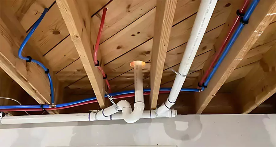 Exposed plumbing pipes and PEX water lines installed in the ceiling of a mobile home.