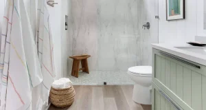 Modern small bathroom remodel with glass shower, light wood flooring, mint green vanity, and woven storage basket — stylish design idea for mobile homes in Huntington Beach, California.