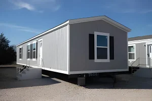 Modern single-wide modular home built by expert mobile home builders in Escondido, featuring gray exterior siding, black shutters, and a clean foundation setup.