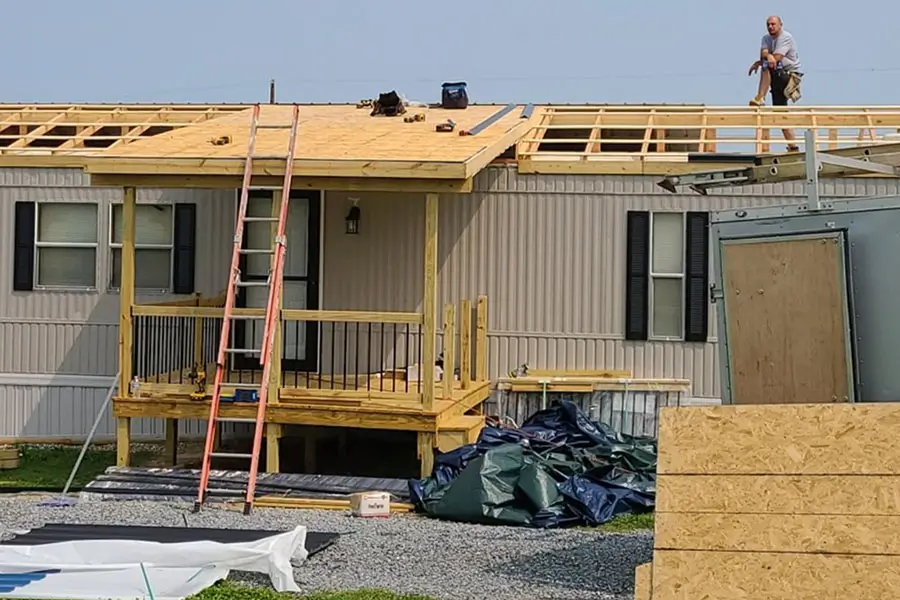 Contractors building a new roof and porch on a mobile home during an exterior renovation project.