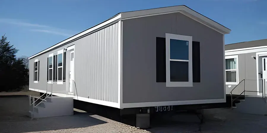 Modern single-wide modular home built by expert mobile home builders in Escondido, featuring gray exterior siding, black shutters, and a clean foundation setup.