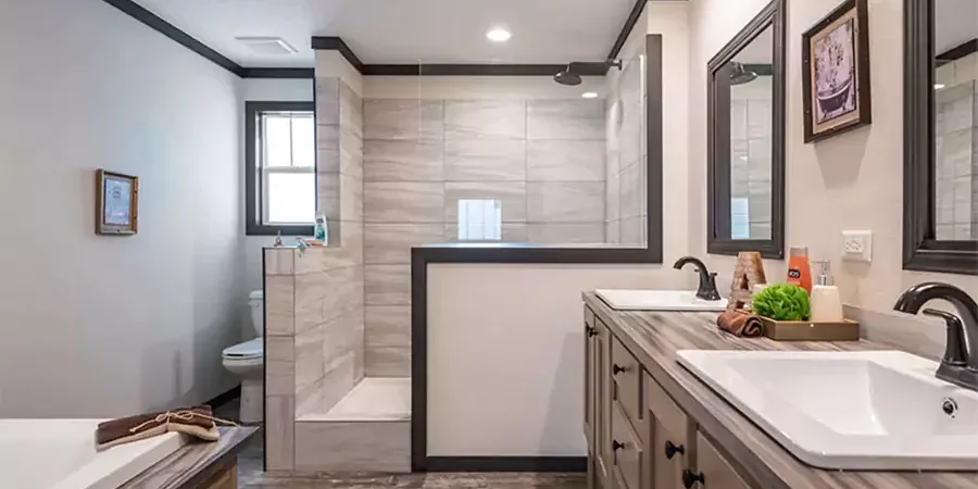 Modern mobile home bathroom remodel in Carlsbad with corner shower, double vanity sinks, framed mirrors, and updated fixtures for maximizing space.